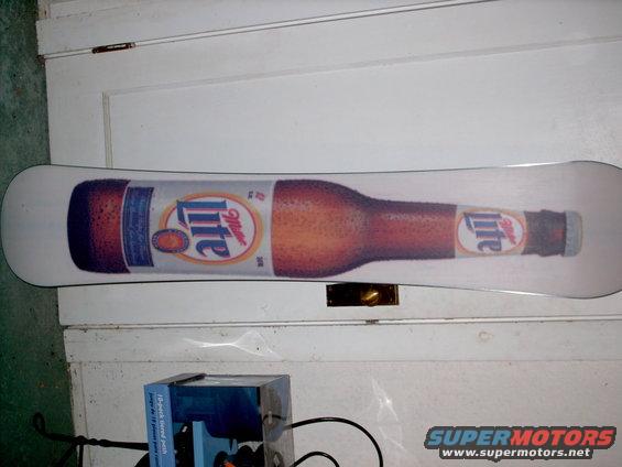 Snowboard with a graphic of a Miller Lite bottle on it, leaning against a white door