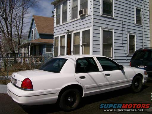White Ford Crown Victoria parked next to a dark SUV in front of a house