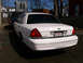 1999 Ford Crown Victoria - The rear of a white 1999 Ford Crown Victoria is visible, its distinctive taillights and license plate.