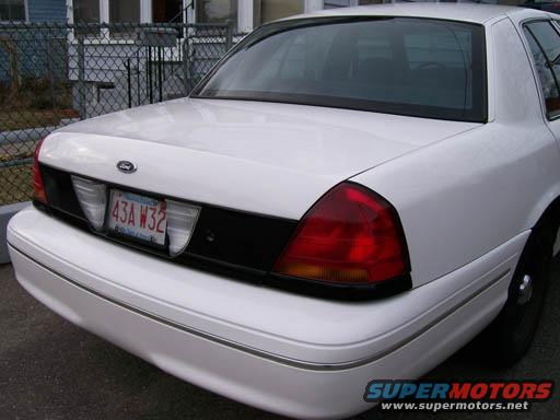 Rear view of a white Ford Crown Victoria with a black trim panel and a Massachusetts license plate