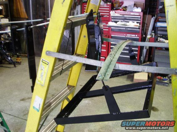 Yellow ladder holding black metal parts, with red tool chests in background