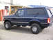 1995 Ford Bronco - A dark blue 1995 Ford Bronco is parked outside a building with a Coca-Cola machine.