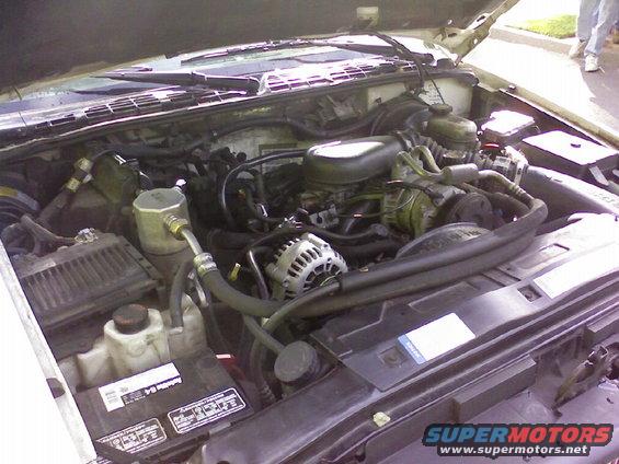 Engine bay with visible alternator, battery, and hoses. White vehicle