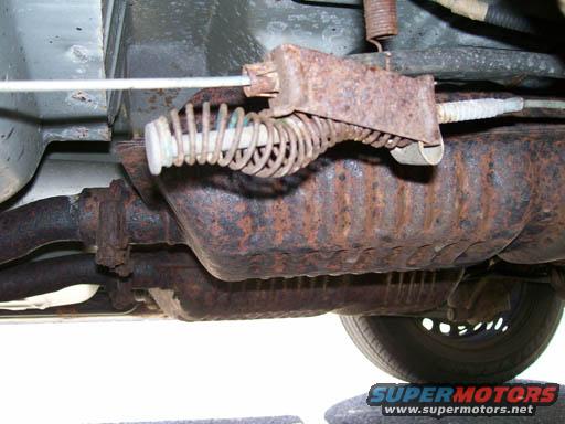 Underbody of a vehicle showing rusted exhaust components and a brake cable mechanism