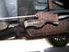1999 Ford Crown Victoria - Close-up view of the underbody of a vehicle, showing a rusty exhaust system and a brake cable mechanism.