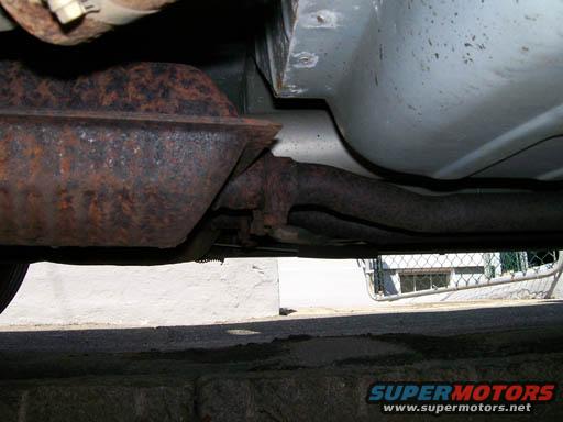 Underbody view of a rusty exhaust system, likely a muffler and pipes