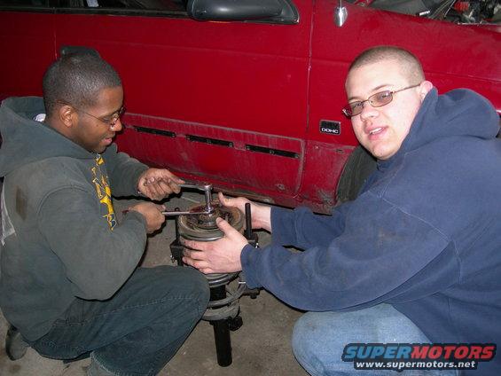 Red car side panel with DOHC badge, two men working on suspension