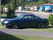 1996 Mazda MX-6 - Side profile of a dark green 1996 Mazda MX-6 coupe parked on a grassy area next to a road.