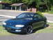 1996 Mazda MX-6 - A 1996 Mazda MX-6 coupe is shown from the front-right angle, parked on a grassy area next to a road.