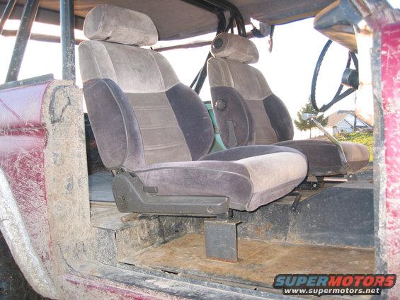 Vehicle interior with two-tone fabric seats, roll cage, and steering wheel. Mud splatters on the door
