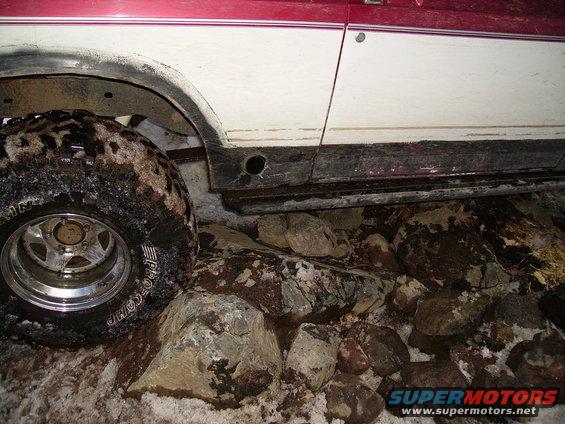 Off-road tire with "PRO COMP" visible, next to a white and red vehicle body over rocks and snow