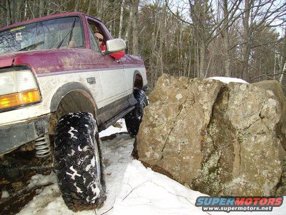 Red and white pickup truck navigating rocky terrain in snow. Visible badge reads '4.9L'