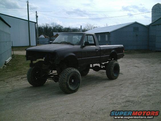 Dark lifted pickup truck with large tires, missing front grille