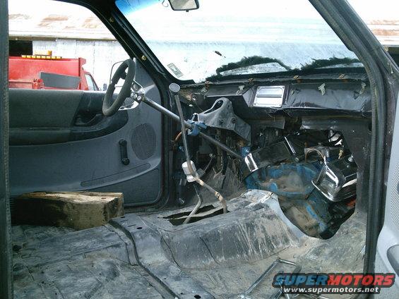 Stripped truck interior with exposed engine components and a block of wood on the floor