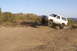 1996 Ford Bronco - A white SUV navigates a dusty off-road trail, its tires kicking up dirt as it climbs a hill.