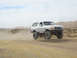 1996 Ford Bronco - Modified Ford Bronco jumps a dirt track in a desert landscape.