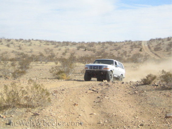 1996 Ford Bronco driving on a dusty desert road, kicking up dust
