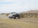 1996 Ford Bronco - A modified Ford Bronco drives off-road, its tires kicking up dust in a desert environment.