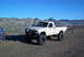 1986 Ford Bronco - A modified white pickup truck sits in a dry, mountainous terrain under a clear blue sky.