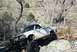 1986 Ford Bronco - A modified white pickup truck is shown off-roading on a rocky trail.