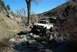 1986 Ford Bronco - A white pickup truck is shown off-roading through a rocky stream bed under a clear blue sky.