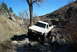 1986 Ford Bronco - Pickup truck off-roading through a rocky stream bed under a clear blue sky.