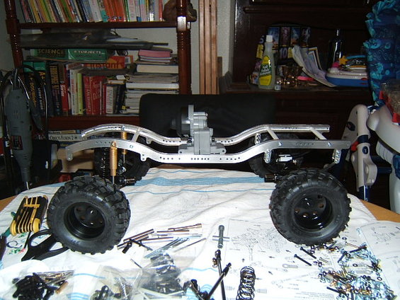 RC crawler chassis with large tires, suspension components, and assembly instructions scattered around
