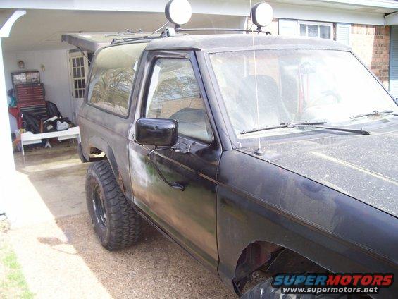1989 Ford Bronco II parked in a driveway, side view. It has aftermarket lights on the roof rack