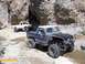1986 Ford Bronco - Two modified off-road vehicles navigate a rocky, narrow canyon path.