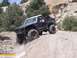 1986 Ford Bronco - Modified Ford Bronco navigates a steep, dusty off-road incline with rocky terrain and sparse vegetation.