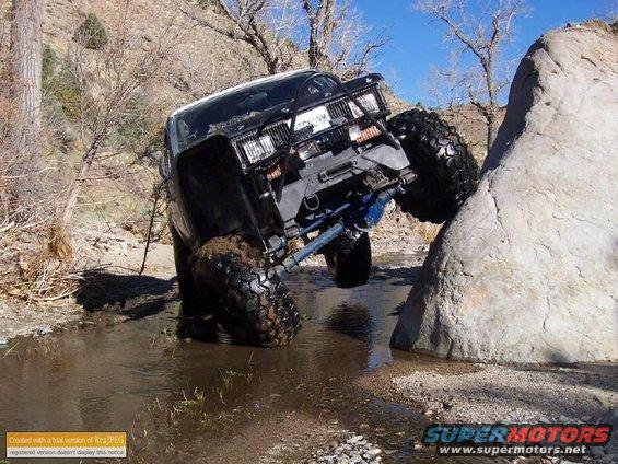 Off-road vehicle with large tires climbing over a rock in a stream bed