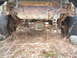 1979 Ford Bronco - The rear axle and fuel tank of a heavily rusted vehicle are visible, surrounded by dry grass and weeds.
