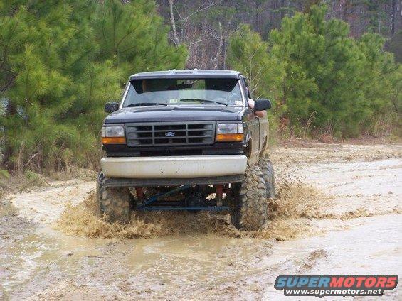 Lifted black pickup truck splashing through a muddy trail