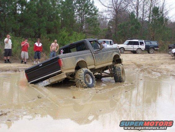 1996 Ford F-150 stuck in a mud pit with people watching; other trucks in background