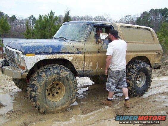 Muddy blue and tan SUV with big tires, two guys talking near the open door