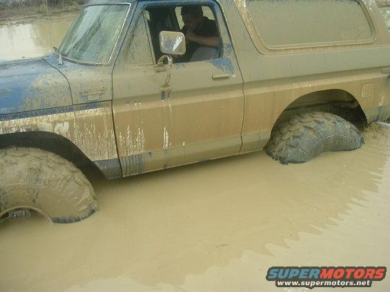 Side view of a mud-covered 1978 Ford Bronco stuck in deep mud