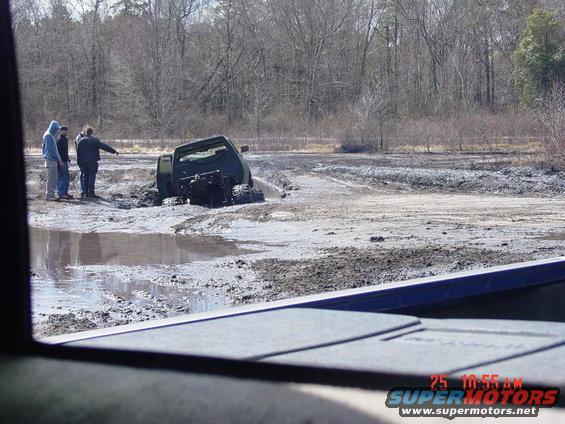 Green 1995 Dodge 1500 stuck in mud, rear wheels submerged, front wheels visible, three people standing nearby