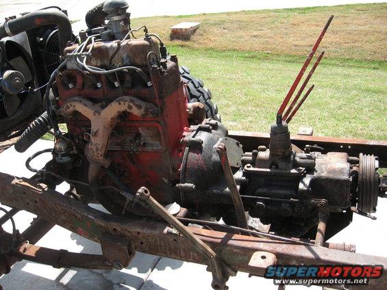 Engine and transmission assembly mounted on a rusty frame. Fan and radiator visible