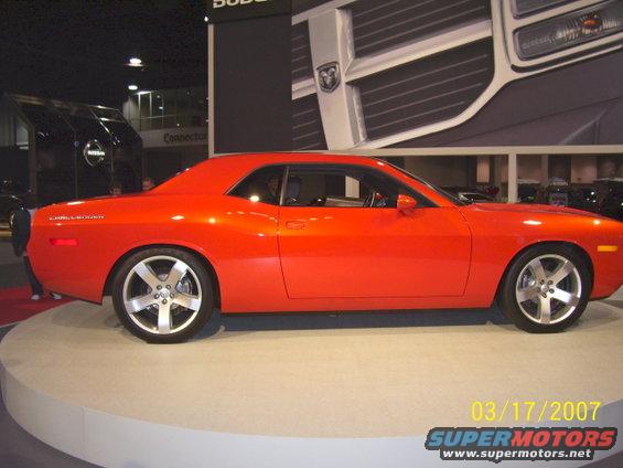 Orange Dodge Challenger parked on a display platform, with a large Dodge logo in the background
