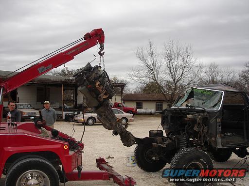Engine being lifted from a dark truck by a red tow truck