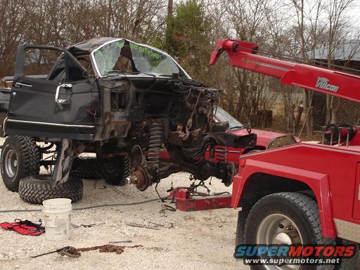 wrecked black SUV with doors open, being lifted by a red tow truck