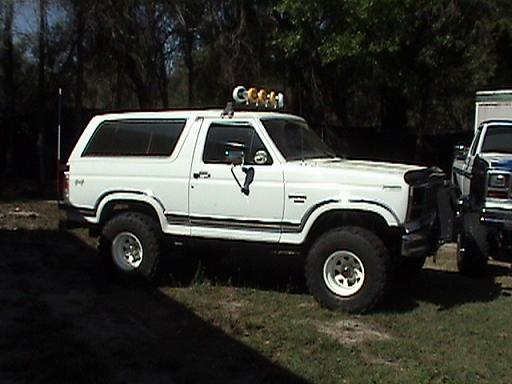 White Ford Bronco with off-road tires, aftermarket bumper, and light bar on roof, parked on grass