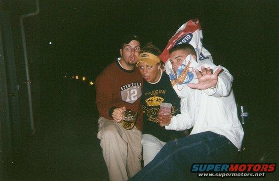 Three people posing for a photo at night, one with a bag over their head