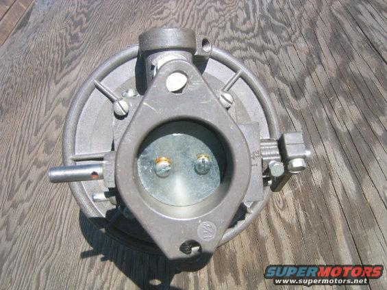 Carburetor with two screws visible inside the opening, mounted on a wooden surface