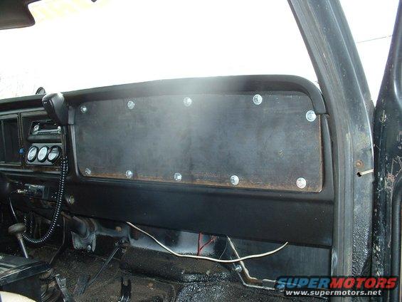 Dashboard of a vehicle with a custom wooden panel screwed over the center console. Gauges are visible to the left