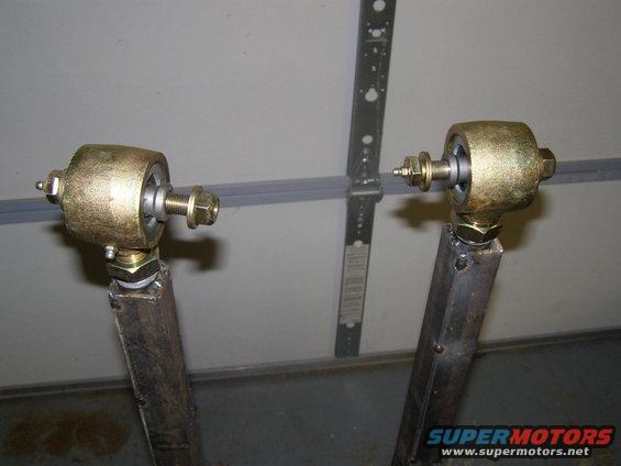 Two gold-colored suspension control arms with bolts and nuts