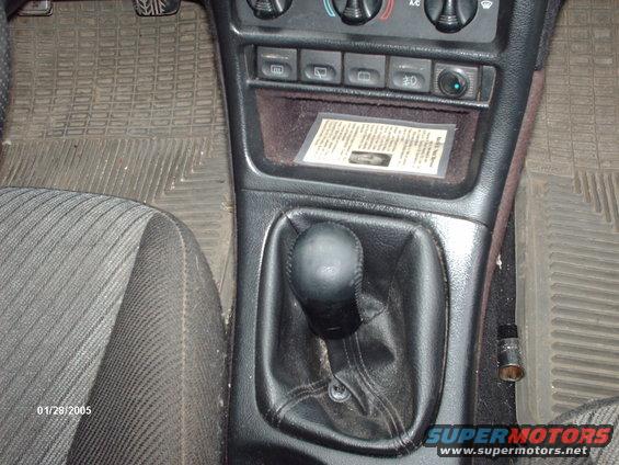 Interior shot of a car's center console with a manual shifter, floor mats, and a small document in the dash