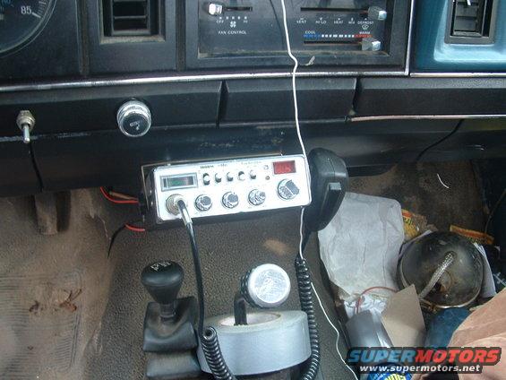 Interior dashboard of a vehicle with a CB radio, gear shifter, and various items on the passenger floor