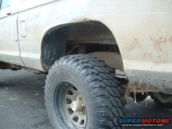 Close-up of a lifted truck's rear wheel well and tire. The body is dirty and shows some rust