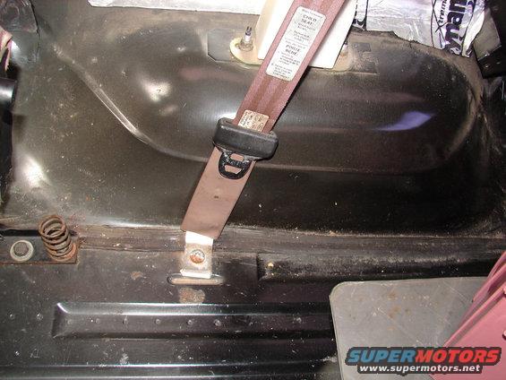 Seatbelt buckle and strap attached to a dark interior panel with visible insulation and a small spring